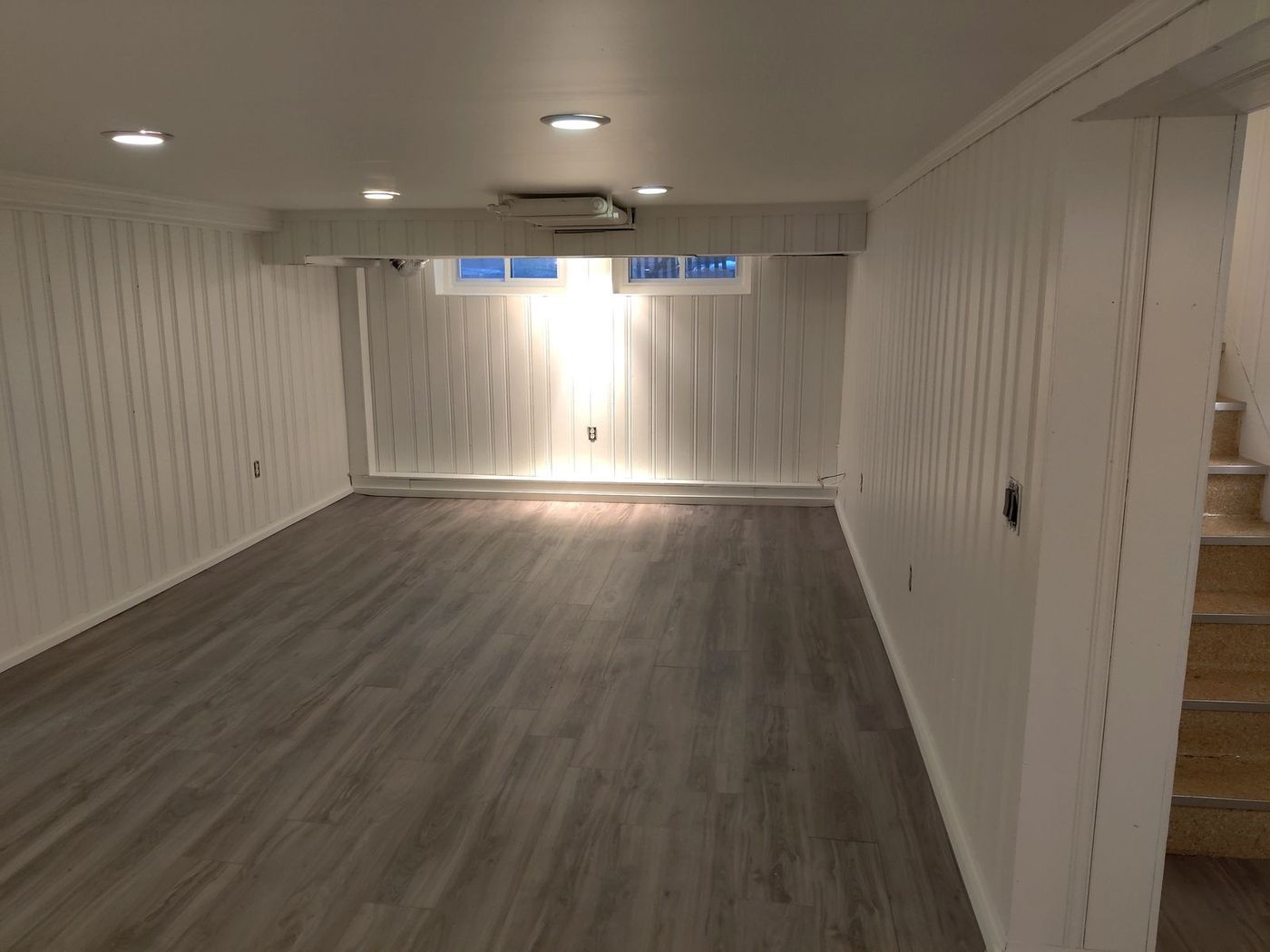 Finished basement with crisp white paneled walls and new plank flooring